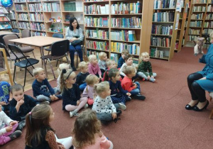 Dzieci siedzą na dywanie i słuchająpani bibliotekarki